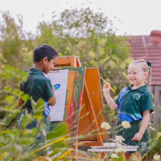 Two students painting at an easel outdoors during a school art activity